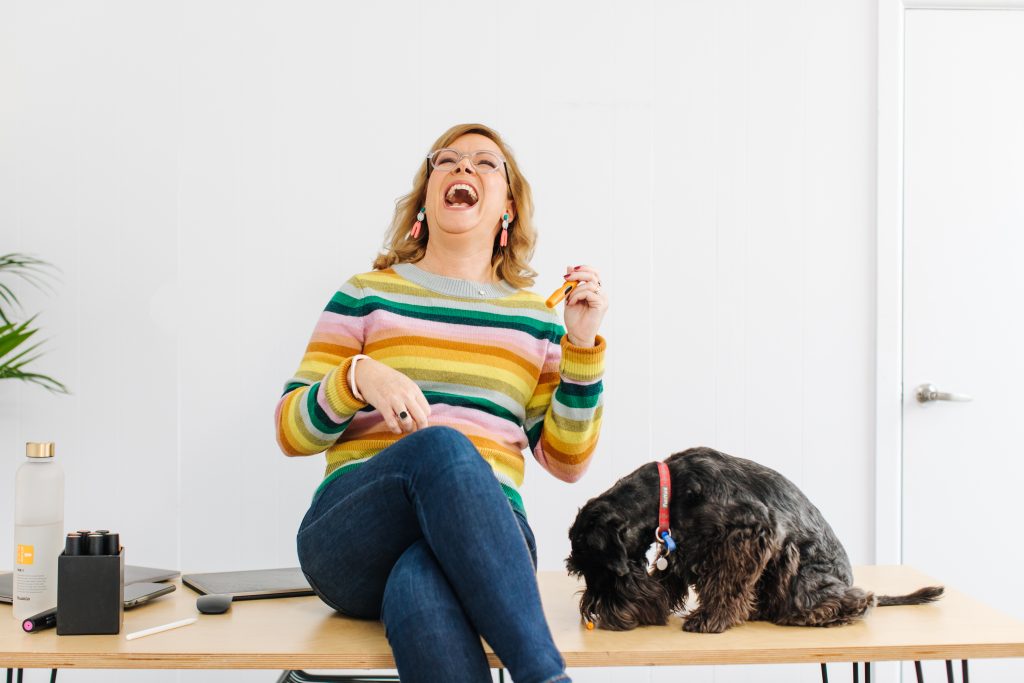 Debbie sitting on a desk with her dog having a really good laugh